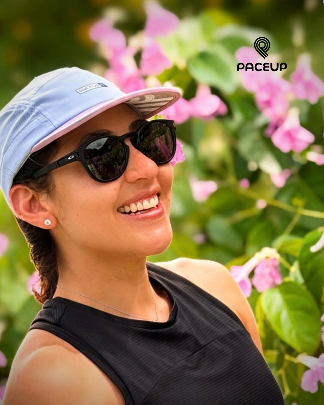 Corredora sonriendo con gorra Paceup celeste entre flores